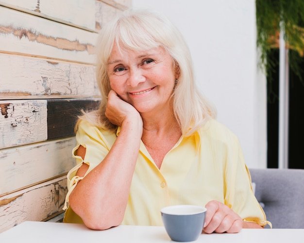 aged-woman-sitting-kitchen-with-cup-smiling_23-2148216451